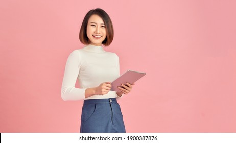 Beauty at work. Confident young women holding digital tablet while standing against pink background