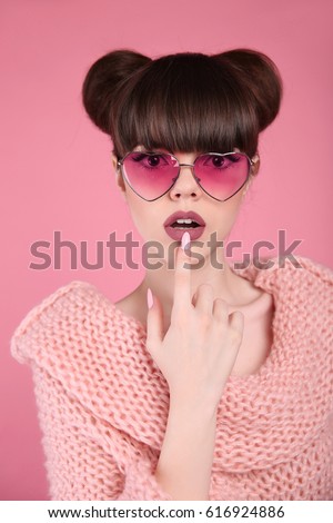 Beauty wow. Fashion surprise teen girl model. Brunette in heart sunglasses with matte lips and hairstyle posing over studio pink background.