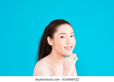 Beauty young Asian woman portrait isolated on blue background touching face. Half naked attractive Asian woman with natural make up, long black hair, black eyes, posing sexy look, smiley face.