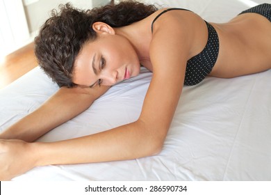 Beauty of a young beautiful exotic sexy woman body laying on a bed at home in black lingerie, thoughtful and moody, relaxing in a bedroom, interior. Health well being aspirational lifestyle, indoors.