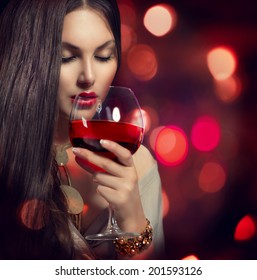 Beauty Young Sexy Woman Drinking Red Wine Over Holiday Blinking Background. Beautiful Girl Takes Glass Of Red Wine Over Night Background. Fashion Glamour Lady Portrait. Wine Tasting