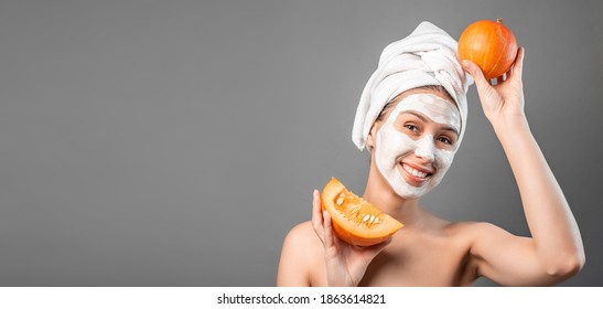 Beauty Young Woman Applying Fresh Treatments With Fresh Sliced Pumpkin Mask On Her Face For Spa Treatment. Portrait Of Young Beautiful Female In Spa While Holding Pumpkin On Face.