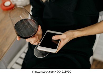 A beauty young woman in a black dress is holding a phone in hands. Girl drink red wine  - Powered by Shutterstock