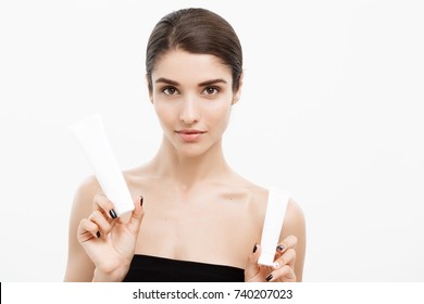 Beauty Youth Skin Care Concept - Beautiful Caucasian Woman Face Portrait Holding And Presenting Cream Tube Product. Beautiful Spa Model Girl With Perfect Fresh Clean Skin Over White Background.