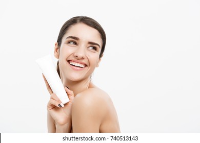 Beauty Youth Skin Care Concept - Beautiful Caucasian Woman Face Portrait Holding And Presenting Cream Tube Product. Beautiful Spa Model Girl With Perfect Fresh Clean Skin Over White Background.