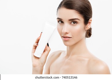 Beauty Youth Skin Care Concept - Beautiful Caucasian Woman Face Portrait Holding And Presenting Cream Tube Product. Beautiful Spa Model Girl With Perfect Fresh Clean Skin Over White Background.