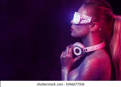 Beautyful girl with glitter and sparkles on her face and body. Portrait of sexy TDJ with headphones and neon sunglasses