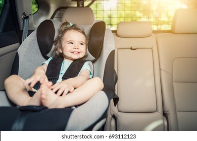 Beautyful Smiling Baby Girl Fastened With Security Belt In Safety Car Seat