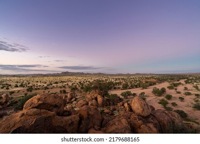 A beautyful Sunset with violet colors in the sky and boulders in the foreground. View of the surrounding desert in Namibia, during the rainy season. Lots of green vegetation. - Powered by Shutterstock