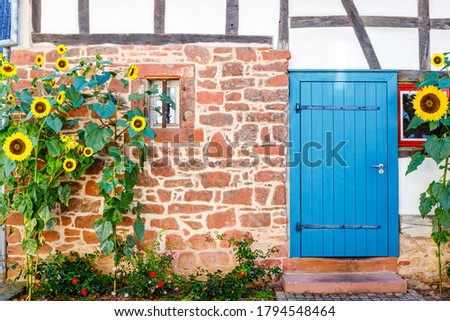 Beautyfull rustic small house with blue wooden small door, windows, Germany. Sunflowers near vintage german house with blue door