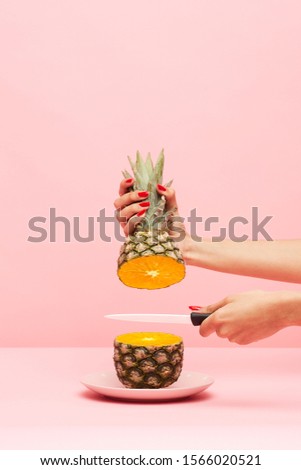 Beautyfull woman's hand with knive cutting a pineapple. The inside appears to be an orange