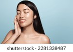 Beauty.Woman applying skincare product on her face. Asian girl with smooth perfect skin, touches her skin with pleased smile, enjoys facial cream rejuvenation effect, stands over blue background