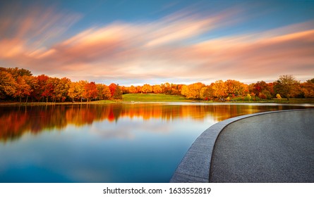 Beaver Lake / Lac Aux Castors in Montreal, Quebec, Canada with Peak Fall Colors and a Vibrant Sunset. The blue sky with streaking, colorful clouds are reflected into the perfectly still lake.