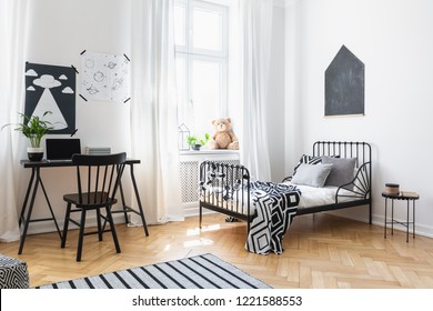 Bed And Black Chair At Desk In Kid's Room Interior With Posters And Plush Toy On Window Sill. Real Photo