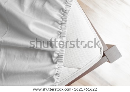 Bed corner with white fitted sheet. White sheet with elastic band. Bed cover.