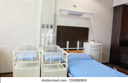 A Bed And Infants Crib Covered By Blue Bed Sheet And Oxygen Tank On White Wall, A Room On Ward For Mother And Babies After Giving A Birth/delivery In Modern Interior Style 