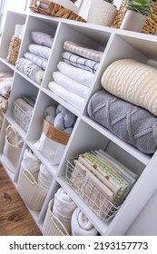 Bed linens neatly folded in white wooden cupboard shelves with potted plants Scandi minimalism method. Bedroom Nordic closet shelf arrangement cotton textile towels sheet duvet cover in boxes cases