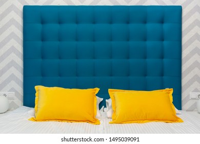Bed With Upholstered Blue Headboard And Two Yellow Pillows