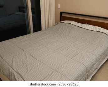 A bed with a white comforter and a black frame. The bed is unmade and the curtains are drawn