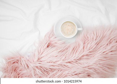 Bedding with a pink fluffy fur plaid and cup of coffee. Copy space. Flat lay, top view