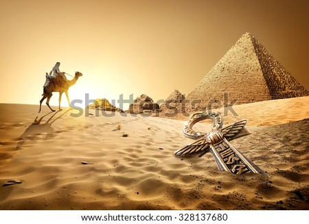 Bedouin on camel near pyramids and ankh in desert