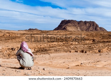 Bedouin in white red scarf in the desert against the backdrop of mountains and blue sky
