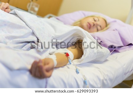 Bedridden female patient lying in hospital bed, receive infusion while recovering after surgery.
