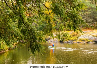 Bedrock Along A Slow Winding River, With Mixed Forest, And A Conifer Frames The View, Backview Of Unidentifiable Man In A Lifejacket Paddles Canoe Down River. Concept