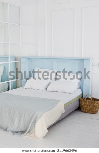 Bedroom with blue bed and white\
pillows. Light cozy bedroom interior with white empty\
walls