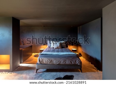 Bedroom with double bed and pillows. To the left of the bed is the bathtub. Romantic and intimate scene. The walls are gray. Nobody inside