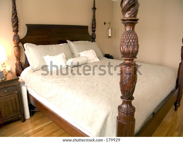 Bedroom with four-poster queen bed, wood floor,\
bedside table and lamp.