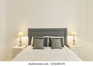 Bedroom headboard upholstered in gray fabric with matching cushions, twin white wooden side tables with lamps and off-white painted walls - Powered by Shutterstock