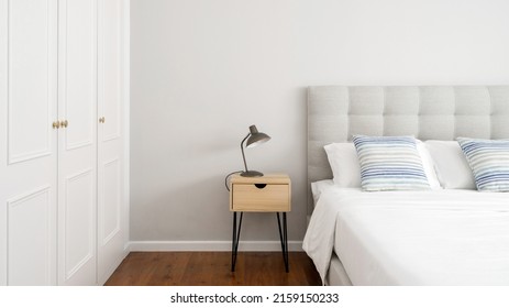 Bedroom interior design in cozy modern house. Web banner view of electric light lamp stand on wooden side table close to bed and wardrobe. Apartment with comfortable furniture