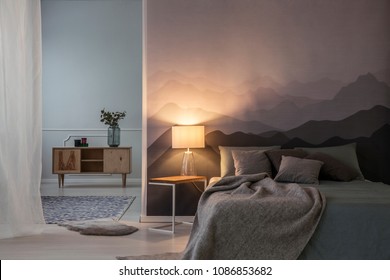 Bedroom Interior At Night With Light. Grey Bedding On Bed Near Wooden Cupboard With Plant