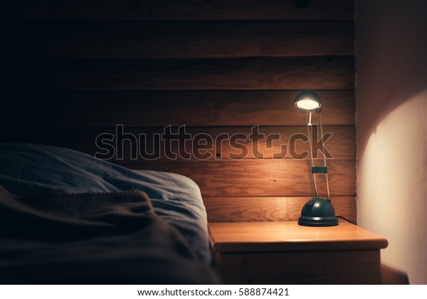 Bedroom lamp\
on a night table next to a sleeping\
bed