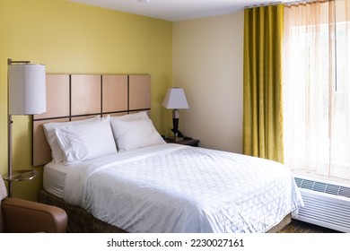 Bedroom room with lamps lights, white pillows with sheet on mattress bed headboard in modern hotel motel room with nobody and window curtains air conditioner