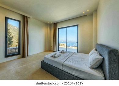 bedroom with a simple bed setup, neutral tones, and large windows providing a scenic view of the ocean and mountains. - Powered by Shutterstock