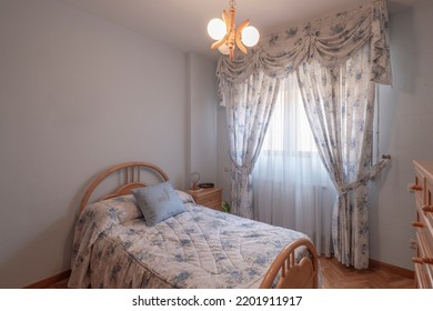 Bedroom With A Single Bed With Wooden Furniture, A Window With Flowery Curtains And A Bedside Table With Drawers