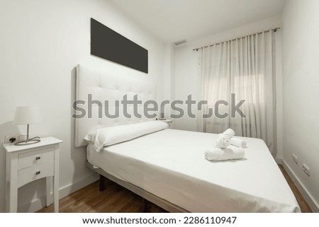 Bedroom with towels on the bed, white capitone upholstered headboard, white bedside tables, window with white curtains and parquet flooring in vacation rental apartment