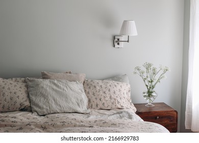 Bedroom View. Striped And Floral Linen Pillows, Blanket. Wooden Night Stand, Bedside Table Blooming Bishops Goutweed Flowers In Glass Vase. Mint, Sage Green Walll With White Lamp. Elegant Interior.