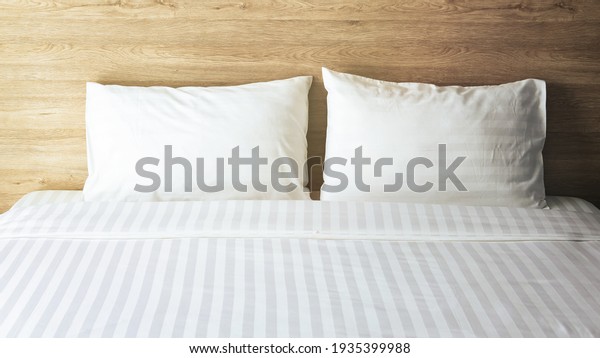 Bedroom with white bed,\
White two pillows, White duvet on the bed with wooden headboard and\
sunlight
