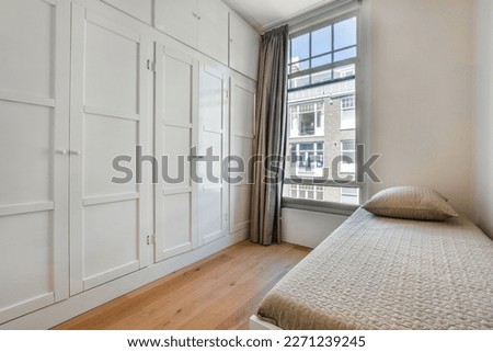 a bedroom with white cupboards and a bed in front of a window that is open to the street outside