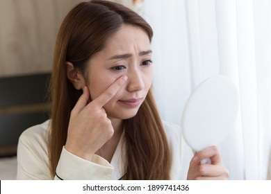 In the bedroom the woman is looking at her eyelids in the mirror. - Shutterstock ID 1899741436