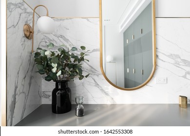 Bedroom working corner decorated with gold stainless mirror and artificial plant in glass vase on gray spray-painted  working table with  marble wall background /apartment interior /copyspace