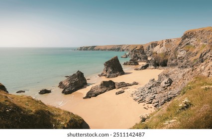 Bedruthan Steps, Cornwall - Scenic coastal landscape with dramatic cliffs, golden sandy beach, and rocky formations against a clear blue sky, rugged natural beauty , British coastline in summer - Powered by Shutterstock