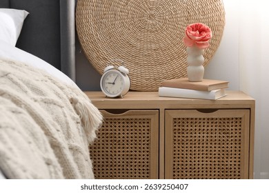 Bedside table with alarm clock, decor and books near bed indoors