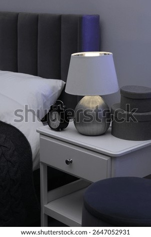 Bedside table with lamp, alarm clock and decor near bed indoors