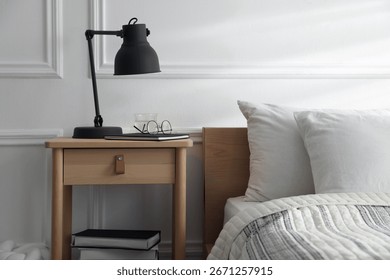 Bedside table with lamp, notebook, glasses, books and glass of water near bed indoors