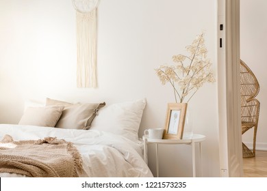 Bedside Table With Mug And Framed Picture Next To Comfortable King Size Bed With Linen Bedding And Beige Blanket, Real Photo