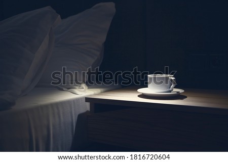 Bedside table with white mug against the bed at night time. Copy paste, nobody